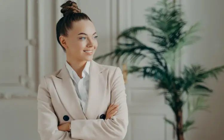 Uśmiechnięta kobieta w beżowej marynarce, z włosami upiętymi w kok. Zastanawia się, co trzeba zrobić, żeby zostać psychologiem.