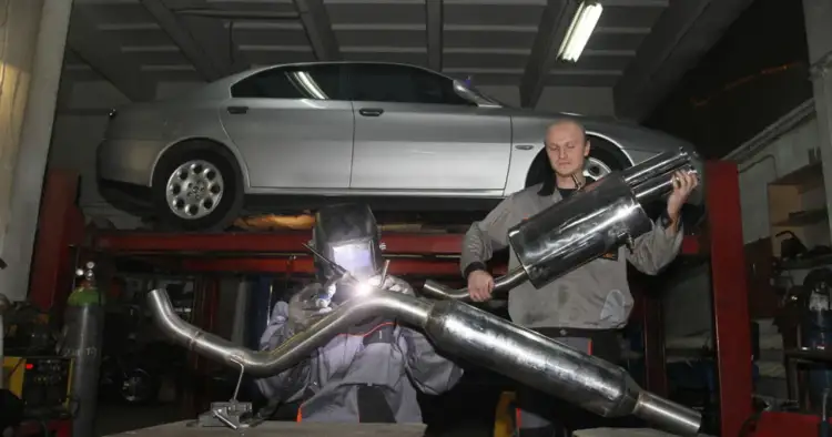 Mechanik spawa układ wydechowy, zastanawiając się, czy downpipe jest legalny. Srebrny samochód uniesiony na podnośniku.