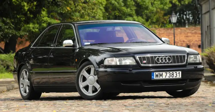 Elegancki, czarny Audi A8 D2 4.2 z lat 90. na brukowanej drodze, otoczony zielenią.