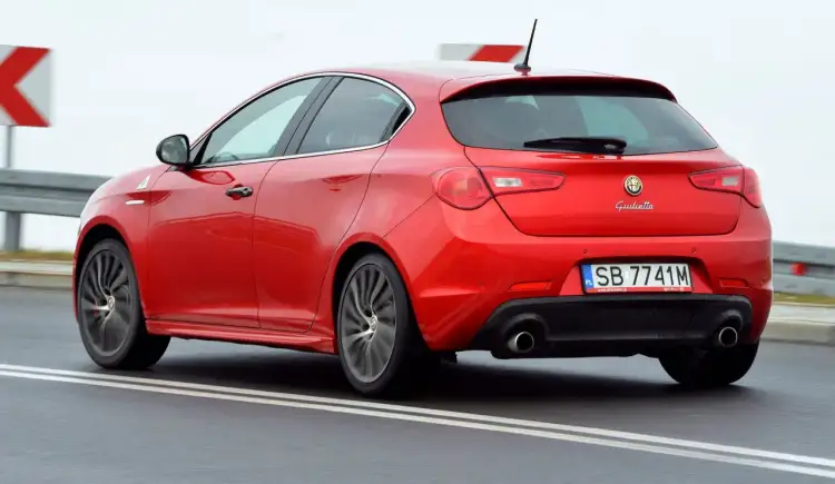 Czerwona Alfa Romeo Giulietta w ruchu drogowym. Wiele osób szuka alfa romeo giulietta opinie przed zakupem.