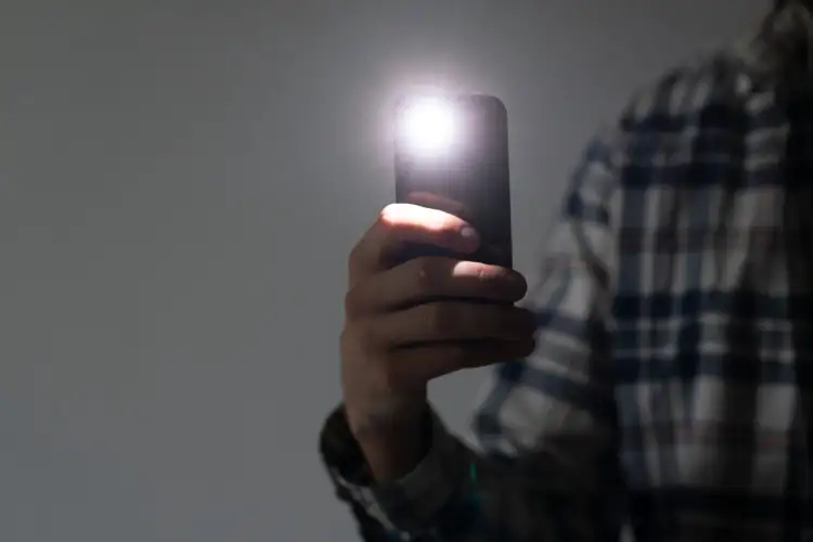 Dłoń trzyma smartfon z włączoną latarką.