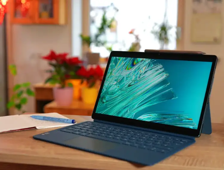 Tablet Lenovo z klawiaturą i rysikiem na drewnianym biurku, obok otwartego notatnika.