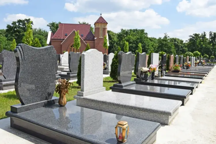 Cmentarz z rzędami nagrobków i budynkiem kościoła w tle.