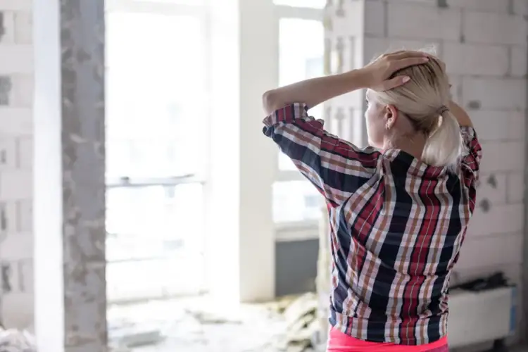 Kobieta z rękami na głowie w niedokończonym domu, zastanawia się, jak zbudować dom.