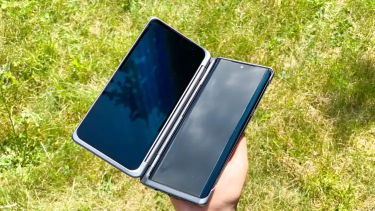 Dłoń trzyma otwarta obudowę LG Velvet Dual Screen na tle zielonej trawy.