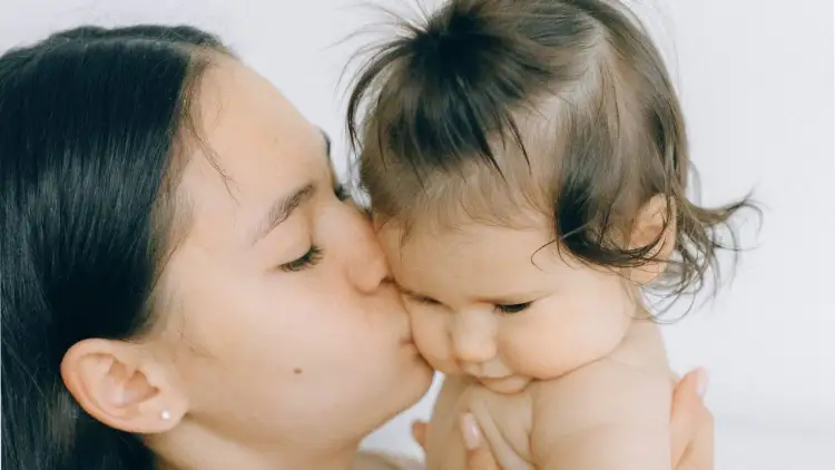 Czułe pocałunki mamy, gdy niemowlakowi rosną włosy. Delikatne kosmyki dziecka kontrastują z ciemnymi włosami matki.