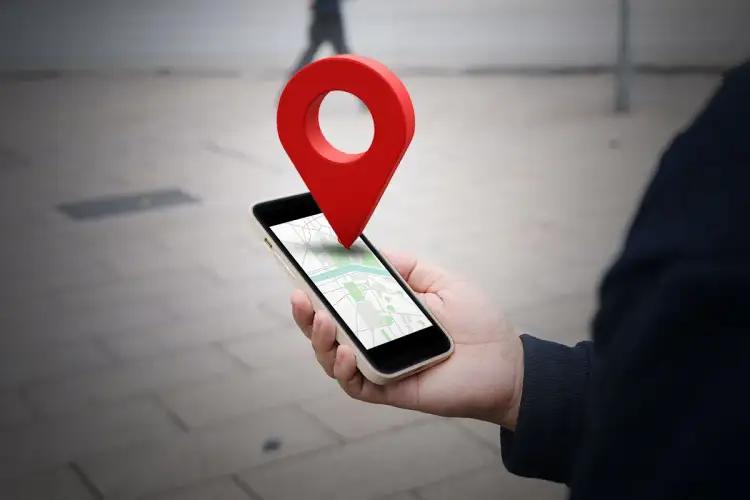 Dłoń trzyma smartfon z mapą, a nad nim unosi się czerwona pinezka. W ten sposób łatwo dowiedzieć się, jak wysłać pinezkę.