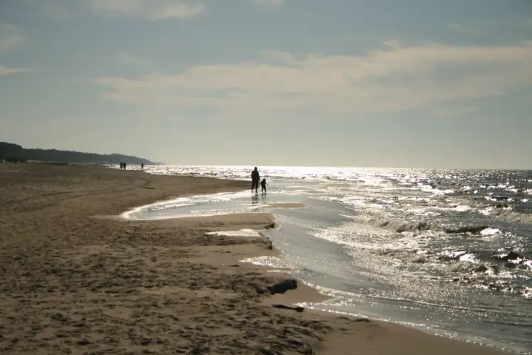 Rodzina spaceruje po plaży, szukając odpowiedzi na pytanie: gdzie najbliżej nad morze z Wielkopolski. Słońce odbija się w falach.