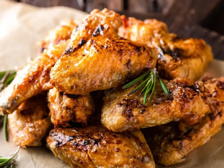 Stos pieczonych skrzydełek z kurczaka, apetycznie przypieczonych, z gałązkami rozmarynu. Ile waży skrzydełko z kurczaka pieczone?