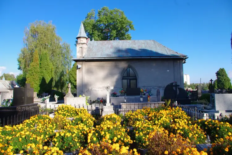 Cmentarz komunalny Oświęcim. Wśród żółtych kwiatów i zieleni widać kaplicę cmentarną i nagrobki.