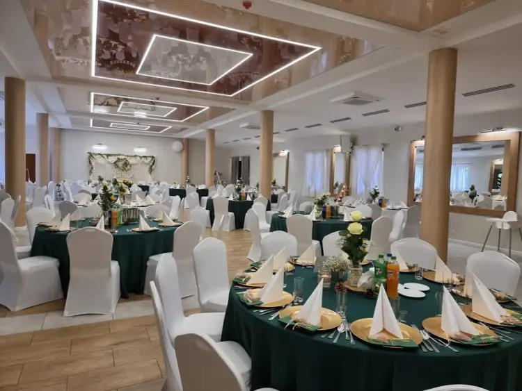 Elegancka sala bankietowa "Rancho pod Bocianem" gotowa na przyjęcie gości. Stoły nakryte zielonymi obrusami, ozdobione kwiatami i złotymi naczyniami.