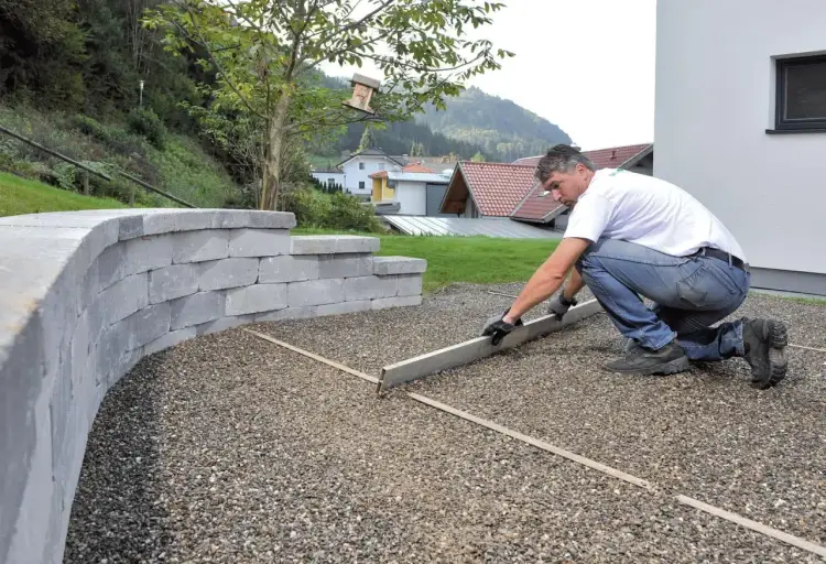 Mężczyzna przygotowuje teren pod budowę podjazdu do garażu z betonu, wyrównując podłoże z kruszywa.