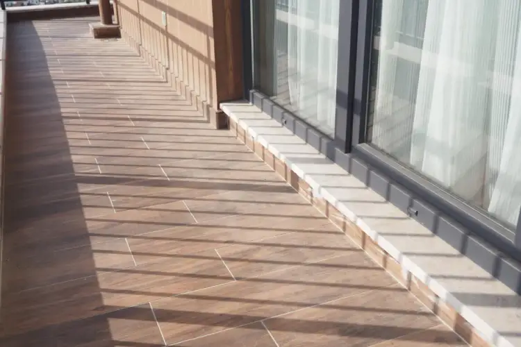 Drewnopodobne płytki na tarasie zewnętrznym, z jasną fugą, tworzą ciepły klimat. Cienie od balustrady dodają uroku.