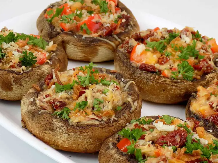 Kilka pieczarek faszerowanych na grilla, z serem, pomidorami i natką pietruszki, gotowych do podania.