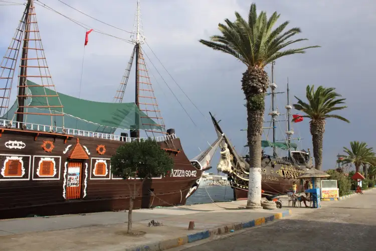 Dwa statki pirackie zacumowane w porcie, palmy i ludzie siedzący przy stoliku. Czy w Tunezji jest drogo?