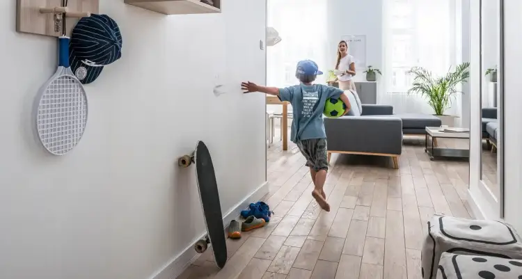 Chłopiec z piłką zostawia ślady na ścianie, co pokazuje, jak ważne jest, by skutecznie umyć ściany przed malowaniem. Obok deska, rakieta i czapka.