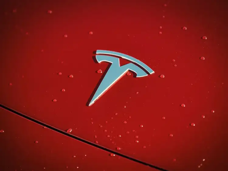 Błyszczące logo Tesli na czerwonej karoserii z kroplami deszczu. Czy Tesla jest tylko elektryczna?