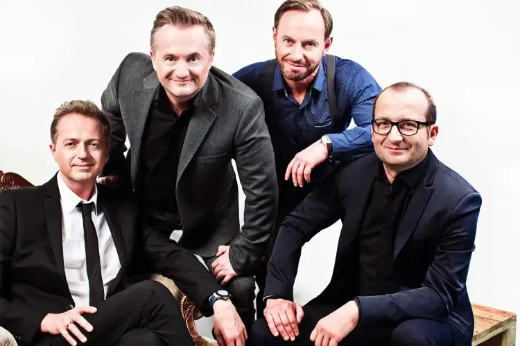 Czterech panów w eleganckich garniturach, którzy występują w Kabarecie Moralnego Niepokoju, pozuje do zdjęcia.