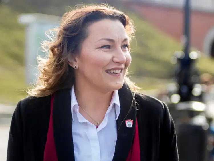 Kobieta w białej koszuli i czarnym płaszczu, uśmiechnięta, patrzy w bok.