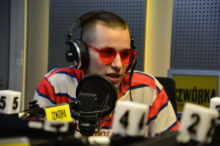 W studiu radiowym siedzi raper, który odpowiada na pytanie: jak ma na imię Żabson? Ma na sobie słuchawki i okulary.