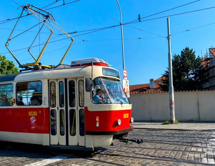 Czerwono-biały tramwaj z numerem 8530 jedzie po brukowanej ulicy. Idealny sposób, by tanio do Pragi pociągiem, a potem tramwajem po mieście.