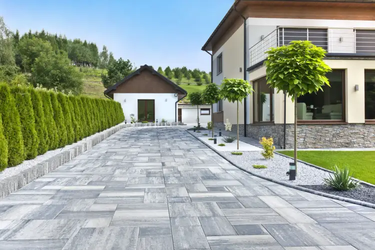 Nowoczesny podjazd przed domem z kostki brukowej, otoczony zielenią i zadbanym ogrodem.