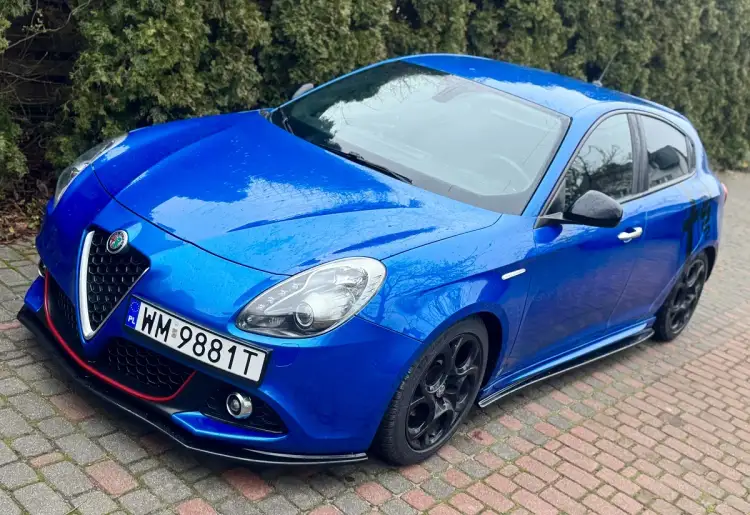 Niebieskie Alfa Romeo Giulietta z agresywnym bodykitem, czarnymi felgami i czerwonymi akcentami na zderzaku.
