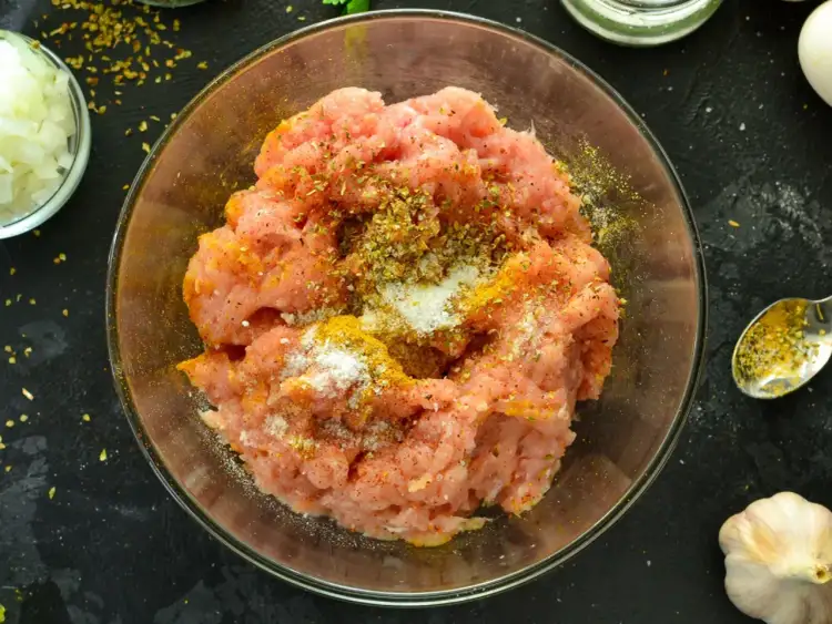 Mielone mięso do kebaba w misce, doprawione przyprawami i solą. Obok posiekana cebula i czosnek.