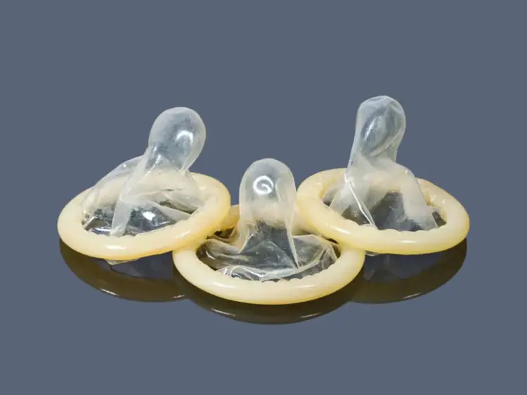 Trzy prezerwatywy bez lateksu, przezroczyste, z żółtym pierścieniem, na ciemnym tle.