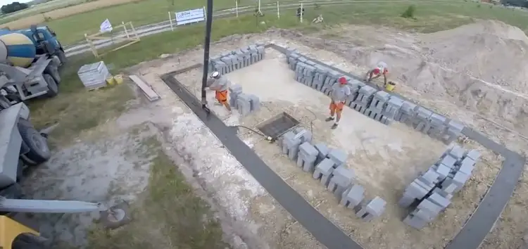 Pracownicy wylewają beton, pokazując, jak wybudować fundamenty. Betonowa pompa i bloczki budowlane na placu budowy.