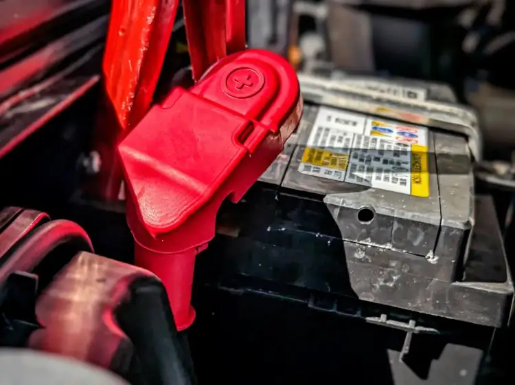 Czerwony zacisk na akumulatorze samochodowym, gotowy do podłączenia, gdy alternator rozładowuje akumulator.