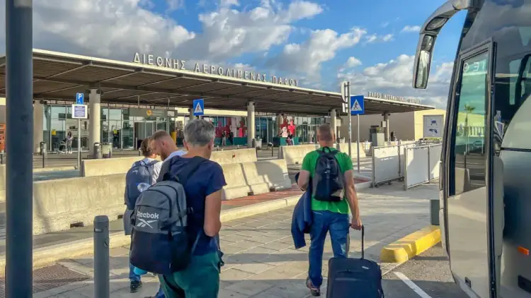 Ludzie z bagażami wychodzą z autobusu na lotnisku w Pafos. Czy na Cyprze jest bezpiecznie? Tak, podróżni bezpiecznie docierają do celu.