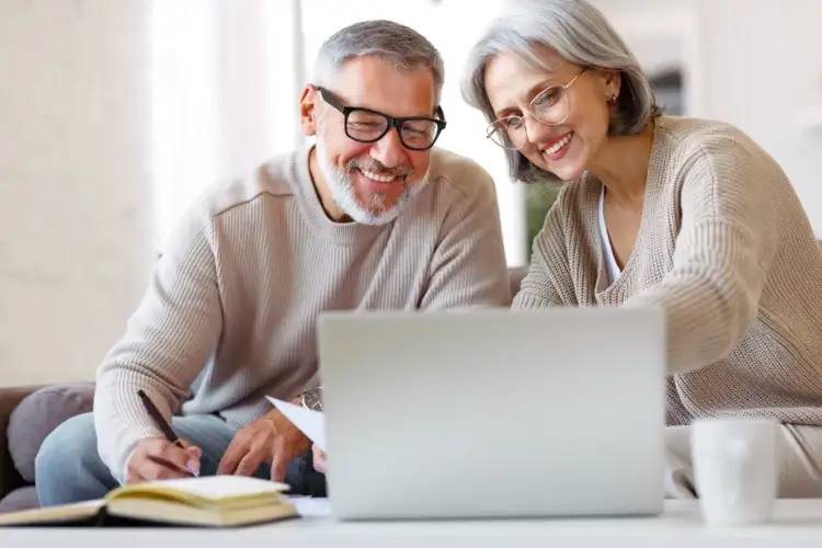 Uśmiechnięci seniorzy przy laptopie, planują przyszłość. Czy emeryt może pracować na cały etat? Oni wiedzą, że tak!