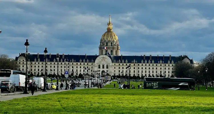 Złota kopuła Les Invalides góruje nad placem w Paryżu. Ruch uliczny i zielony trawnik tworzą tło dla tego historycznego miejsca.