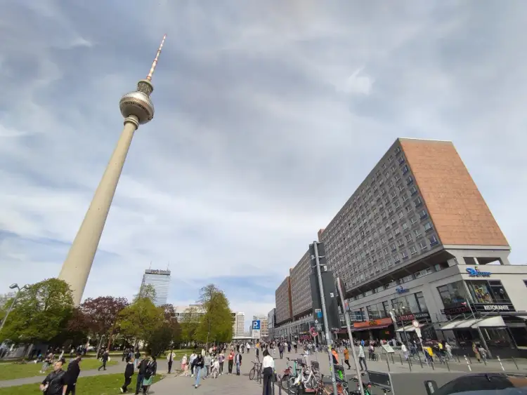 Wieża telewizyjna Berlin góruje nad placem pełnym ludzi, rowerów i budynków.