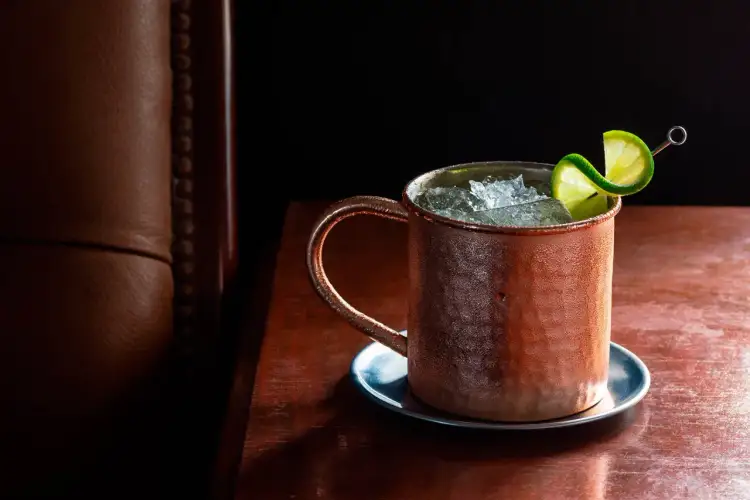 Chłodny Moscow Mule lub London Mule w miedzianym kubku, ozdobiony plasterkiem limonki, na drewnianym blacie.