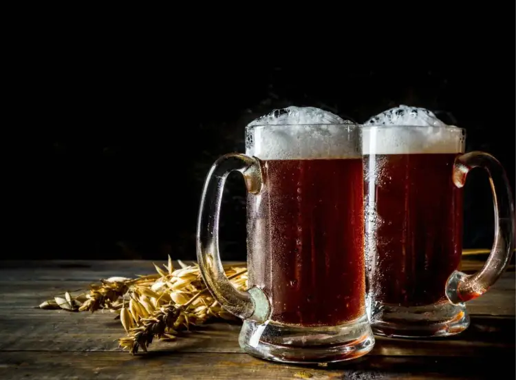 Dwa kufle ciemnego piwa z pianką, obok kłosy zboża. Zastanawiasz się, ile może stać otwarte piwo?