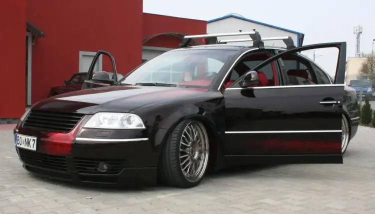 Czarny Passat B5 z body kitem i czerwonymi wstawkami, otwarte drzwi, czerwone wnętrze, relingi dachowe.