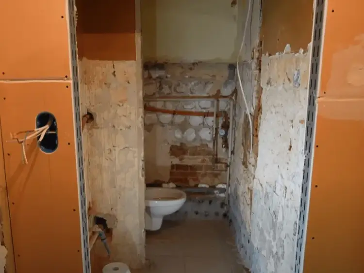 Remont łazienki w toku. Widać białą muszlę klozetową i instalacje. Ściany przygotowane pod płytę GK do łazienki.