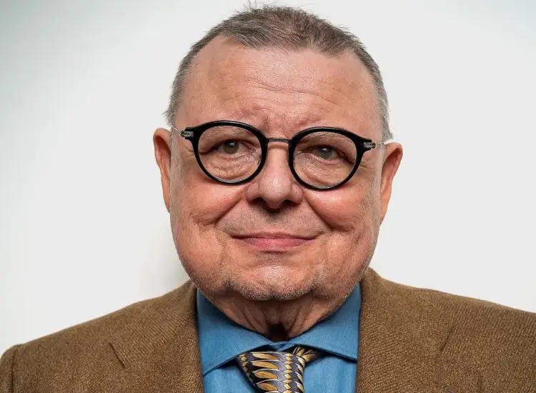 Uśmiechnięty Wojciech Mann w okularach i brązowej marynarce. Ile lat ma Wojciech Mann? Tego nie dowiemy się ze zdjęcia, ale wygląda na doświadczonego i pełnego życia.