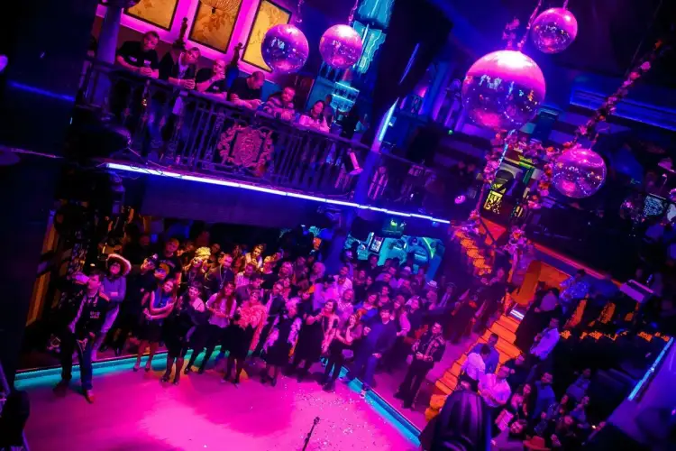 Tłum ludzi bawi się w klubie Capitol w Warszawie, wśród migoczących kul dyskotekowych i neonowego światła.