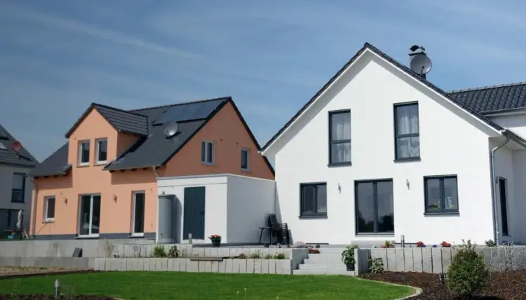 Dwa nowoczesne domy, jeden brzoskwiniowy z panelami słonecznymi, drugi biały. Idealne do ubezpieczenia domu w budowie.