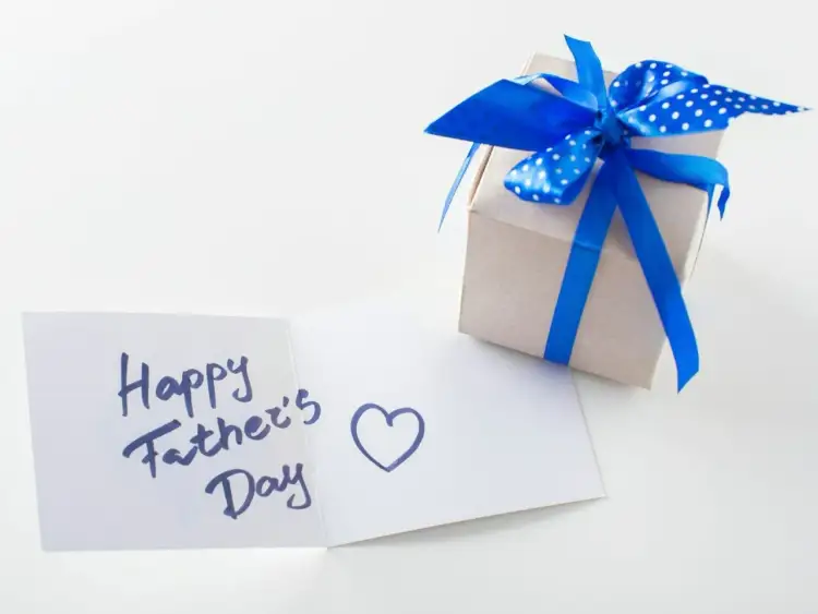 Prezent na Dzień Ojca: kartka z życzeniami "Happy Father's Day" i sercem, obok pudełko ozdobione niebieską wstążką w kropki.