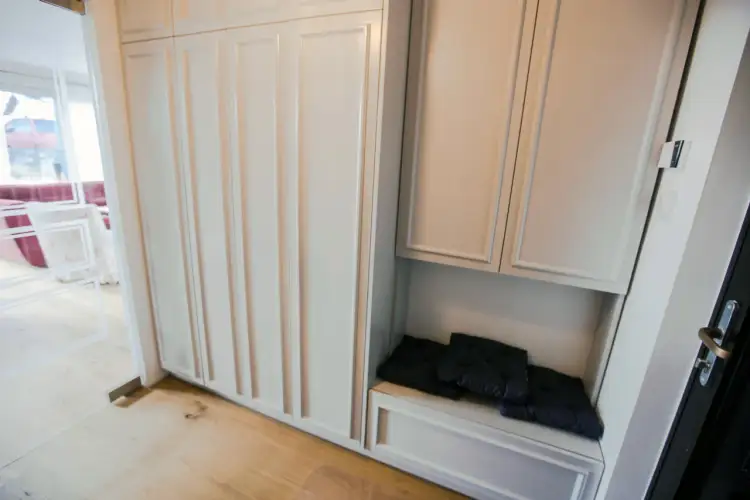 Biała szafa z ozdobną sztukaterią na frontach. Wnęka z czarnymi poduszkami do siedzenia.