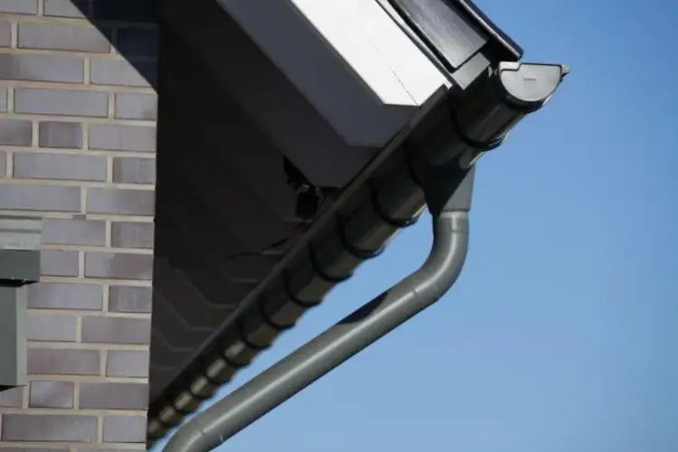 Szare rynny tytan cynk odprowadzają wodę z dachu domu z cegły.