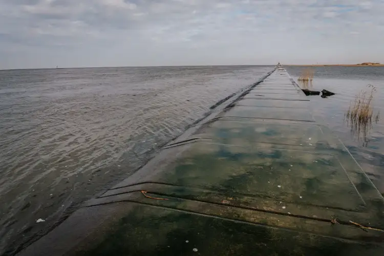 Betonowy falochron prowadzi do miejsca, gdzie Wisła wpada do morza. Woda faluje, a niebo jest zachmurzone.