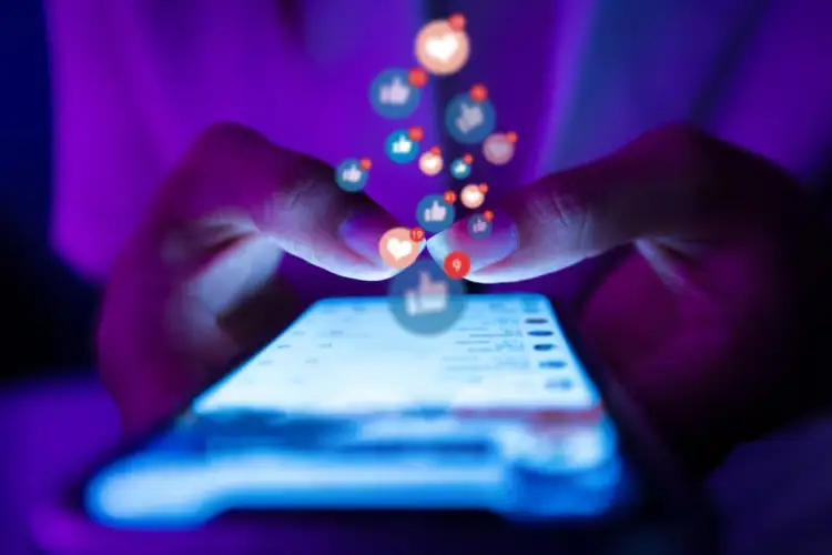 Palce na ekranie smartfona, nad nimi unoszą się ikony polubień i serduszek. Tak można zacząć szukać kogoś na FB po Instagramie.