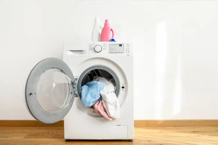 Pranie parowe w pralce: biała pralka z otwartymi drzwiczkami, w środku kolorowe ręczniki. Na górze dwie butelki z płynem do prania.