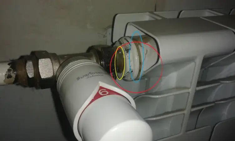 Uszczelnienie cieknącego grzejnika: widoczny zawór termostatyczny i miejsce połączenia z grzejnikiem, które wymaga naprawy.