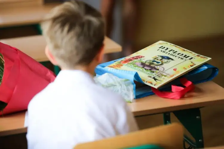 Chłopiec w białej koszuli siedzi przy ławce, na której leży dyplom z sową. Czy zachowanie liczy się do średniej?